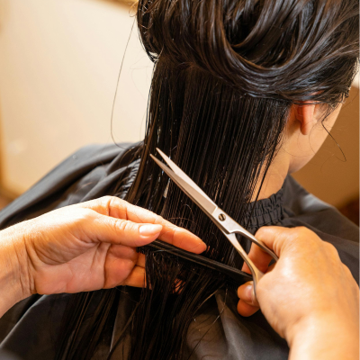 Cabeleireiro cortando o cabelo molhado de uma pessoa, segurando as mechas com os dedos e utilizando uma tesoura de corte profissional.